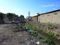 Absence d'assainissement à Cap-Haïtien, Haïti : les déchets à même le sol (incluant des sacs plastiques remplis d'excréments) bloquent les canaux de drainage qui débordent à la moindre pluie, et endommagent les infrastructures riveraines (routes, bâtiments…).